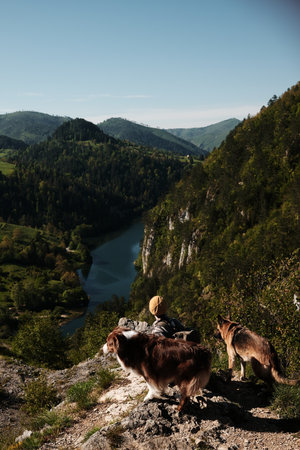 Woman sitting on edge with two dogs - German and Australian shepherd, admiring spring view of canyon...