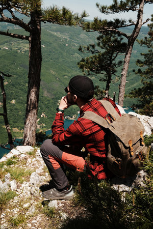 Man sitting on a rocky ledge surrounded by pine trees, enjoying an elevated view of the Drina river and mountains in Tara National Park. Travel in Serbia country conceptの写真素材