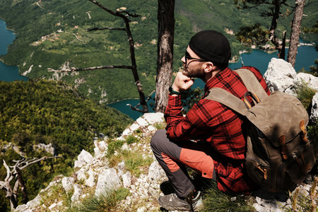 Man sitting on a rocky ledge surrounded by pine trees, enjoying an elevated view of the Drina river...