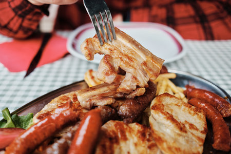 Fork holding a juicy grilled meat piece from a traditional Serbian mixed grill platter. Balkan cuisineの写真素材
