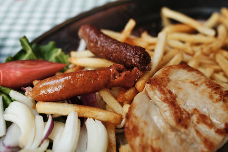 Close-up of a traditional Serbian grilled meat platter with sausages, pork and French fries served on a metal plate. Balkan cuisineの写真素材