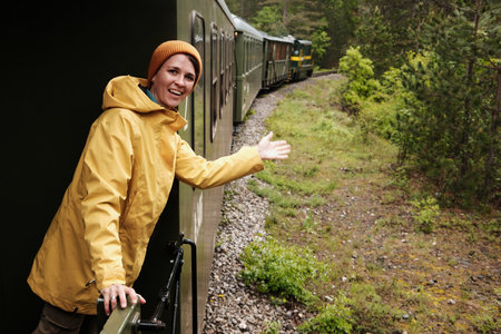 A cheerful woman gestures towards the curving Shargan - Sargan Eight train in a scenic wooded...