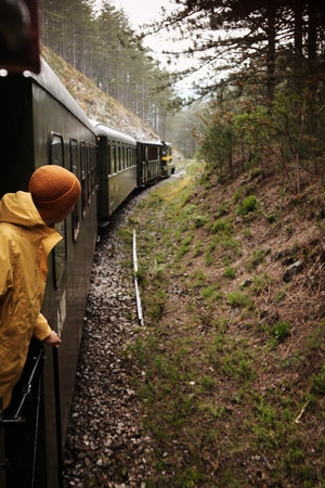 A woman in yellow outerwear leans out from the train, admiring the mountainous landscape and winding railroad of the Shargan Eight. Serbia in spring season. Travel conceptの写真素材