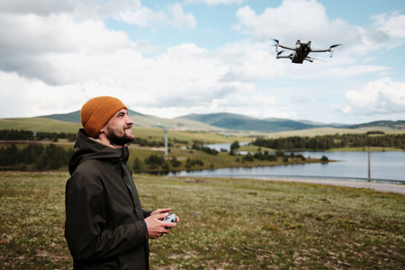 Man flying a drone above Ribnicko Lake in Zlatibor, Serbia. A scenic spring day with hills and water in the background. Travel blogger making video outdoor. Side view portrait.の写真素材