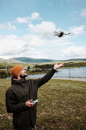 Smiling man reaching for a drone in mid-air above a lake in Zlatibor, Serbia. Beautiful spring...