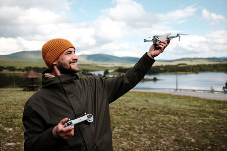 Man landing a drone by hand with a big smile, Ribnicko Lake and green hills in the background....