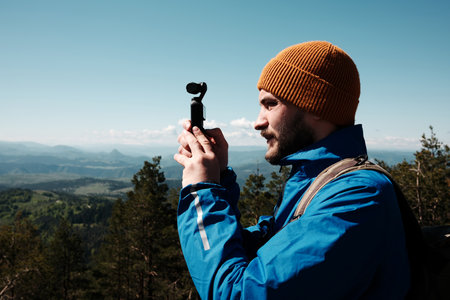 Man filming scenic mountain view with a compact gimbal camera on a sunny spring day in Zlatibor, Serbia. Travel blogger making video outdoorの写真素材