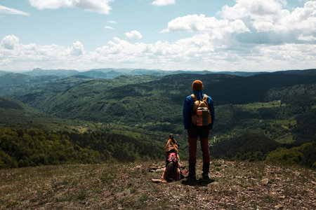 Male hiker and German Shepherd dog standing at a scenic viewpoint, gazing at the vast green valley of Cigota mountain. Rear view. Travel with pet conceptの写真素材