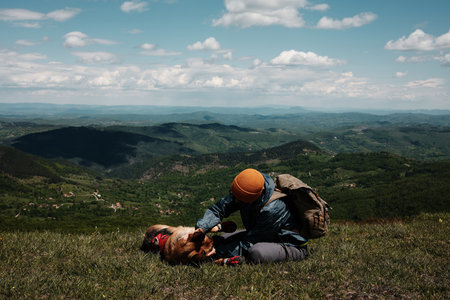 Female hiker cuddling with German Shepherd dog on a grassy mountain slope, with panoramic view of Zlatibor mountains in Serbia. Travel with pet concept.の写真素材