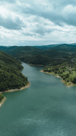 Aerial view of Rovni Lake surrounded by lush green hills and rural villages in western Serbia,...