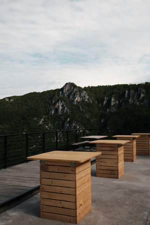 Modern wooden tables on a panoramic terrace with a view of dramatic rocky cliffs covered in forest...