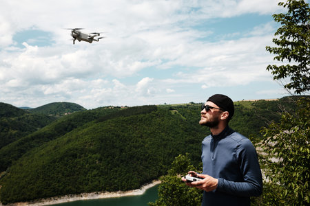 Man with sunglasses controls a flying drone in the Serbian countryside during spring. He stands near...