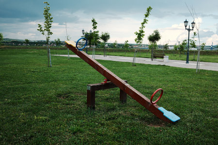 Bright wooden seesaw in a park with scenic background and cloudy sky.
