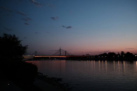 Orange-lit bridge over the Sava River in Belgrade at sunset, reflecting beautifully on calm water under the evening skyの写真素材