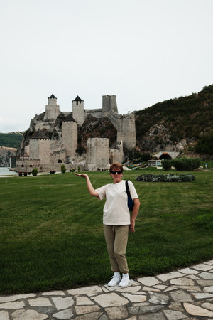 Smiling woman playfully posing with outstretched hand in front of Golubac Fortress in summer time. Travel in Serbia conceptの写真素材