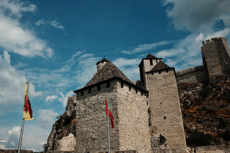 Imposing view of Golubac Fortress with stone towers, battlements, and red flags under a vibrant blue sky. A stunning medieval landmark on the Danube River in Serbiaの写真素材