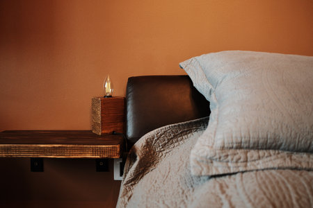 Close-up of a modern wooden bedside shelf with a minimalist lamp and gray bed linen in a cozy bedroomの写真素材