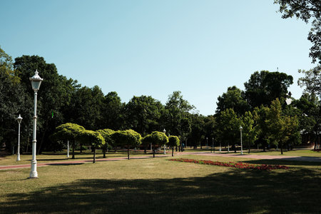 Lush green park in Palic, Serbia with trimmed trees, grass, flowerbeds, and decorative street lamps...