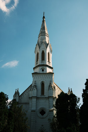 White gothic-style church tower with detailed spire and cross in Zrenjanin, Serbia. Bright sky and architectural contrast enhance the historic feel of the landmarkの写真素材