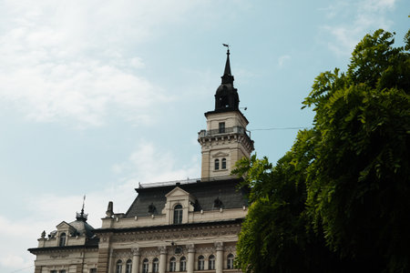 Close-up of the tower and roof details of Novi Sad City Hall, Serbia, with dramatic sky and green...
