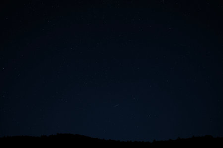 Night sky filled with stars above mountain ridges, peaceful astrophotography view of constellations