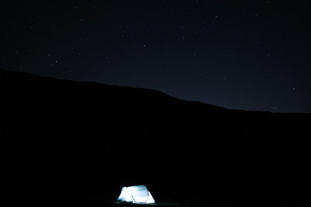 Illuminated camping tent under a starry night sky with visible meteors, creating a peaceful outdoor astrophotography scene. Outdoor travel conceptの写真素材