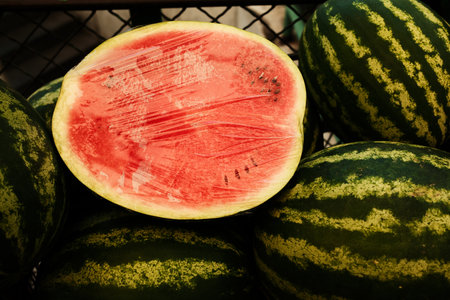 Fresh half watermelon wrapped in plastic film at the market. Juicy red fruit with green striped...