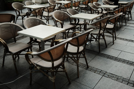 Outdoor cafe with empty wicker chairs and square tables arranged on stone pavement, urban dining...