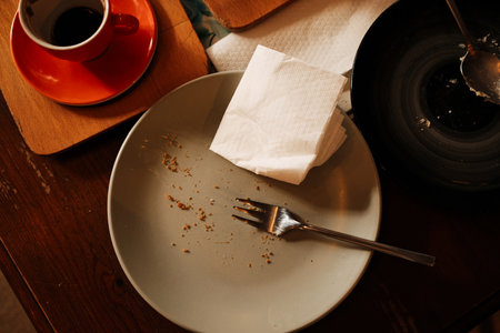 Close-up of empty plate with crumbs and fork on cafe table after eating dessert, coffee cup nearby. Top viewの写真素材