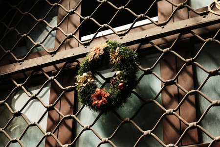 Decorative Christmas wreath with flowers and pinecones hanging on a barred windowの写真素材