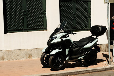 Modern three-wheeled scooter with black seat parked on urban sidewalk in sunlight. Belgrade, Serbiaの写真素材