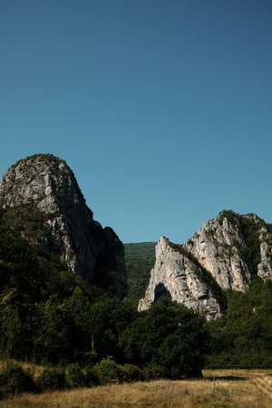 Majestic rocky peaks rising above dense green forest under a clear blue sky in Stara Planina, Serbiaの写真素材