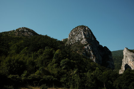 Majestic rocky peaks rising above dense green forest under a clear blue sky in Stara Planina, Serbiaの写真素材