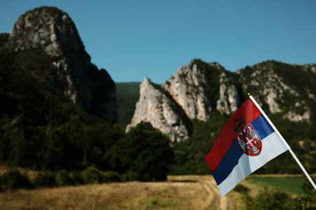 A Serbian flag waving proudly in front of dramatic mountain cliffs under a clear blue sky. Stara planina national parkの写真素材