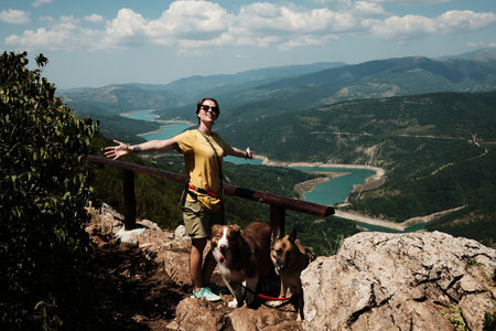 Woman spreading arms in joy with dogs German and Australian Shepherd on mountain viewpoint, stunning...