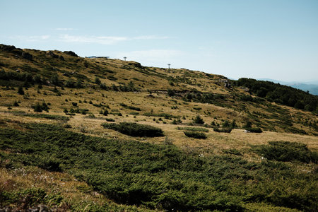 Open grassy plateau of Stara Planina with scattered rocks and distant ski lift under summer sky....