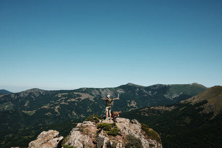 Person with a dog standing on a rocky peak of Stara Planina, enjoying panoramic mountain views under a clear blue sky. Rear view.の写真素材