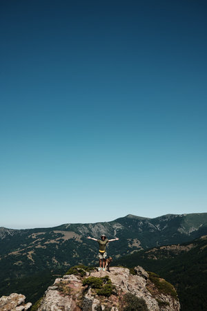 Female hiker with arms wide open standing on a rocky mountain top of Stara Planina with german shepherd dog, nature and freedom concept. Travel and hiking with pet conceptの写真素材
