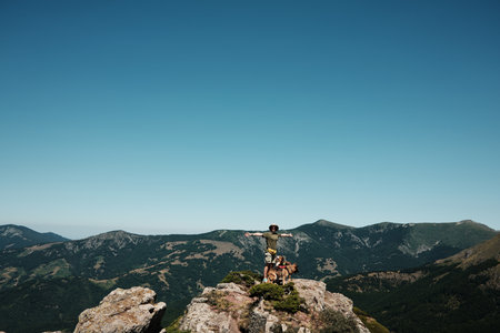 Female hiker with arms wide open standing on a rocky mountain top of Stara Planina with german shepherd dog, nature and freedom concept. Travel and hiking with pet conceptの写真素材