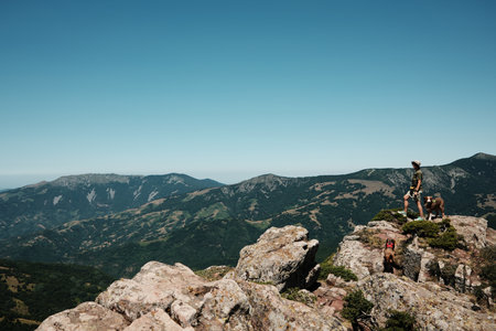 Woman with two dogs German and Australian Shepherd standing on rocky cliffs of Stara Planina, overlooking vast mountain valleys and dramatic landscapes. Travel and hiking with pets conceptの写真素材