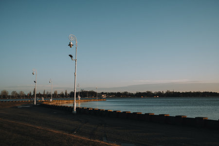 A quiet winter evening at Palic Lake promenade in Serbia, with vintage street lamps casting long...