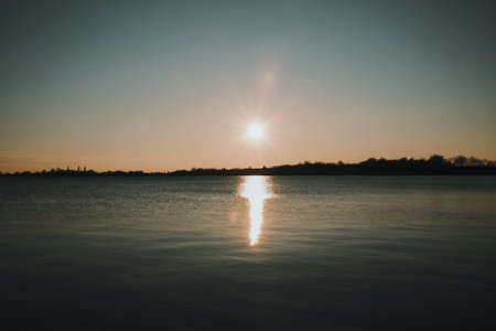Stunning sunset over Palic Lake in Serbia, with the sun casting golden reflections across the peaceful winter waterの写真素材