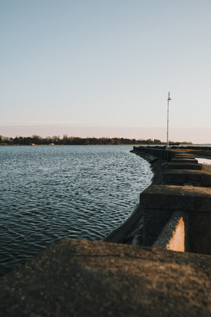 A quiet winter evening at Palic Lake promenade in Serbia, with vintage street lamps casting long shadows over the calm waterの写真素材