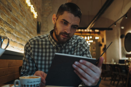 Man in a cozy cafe reading a menu with a cup of coffee on the table. Warm lights and rustic brick wall create a relaxed moodの写真素材