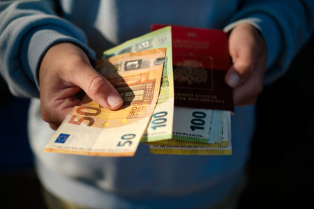 Person holding Russian passport with euro banknotes, showing 50, 100 and 200 euro bills in hand. The...
