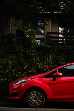 Red car parked near green ivy-covered residential building in Belgrade, side view close-upの写真素材