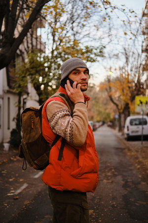 Man with backpack talking on phone in calm autumn street, Belgrade