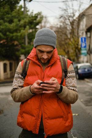 Man in red vest standing on street using smartphone in autumn city. Front view