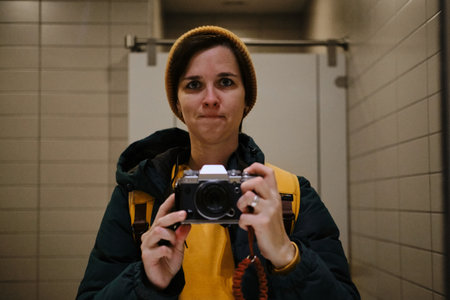 Woman in yellow beanie and jacket taking a mirror selfie with a retro camera