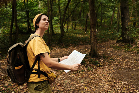 Woman with backpack holding map in Fruska Gora forest, Serbia. Hiking trail exploration in national park. Female tourist outdoor portraitの写真素材